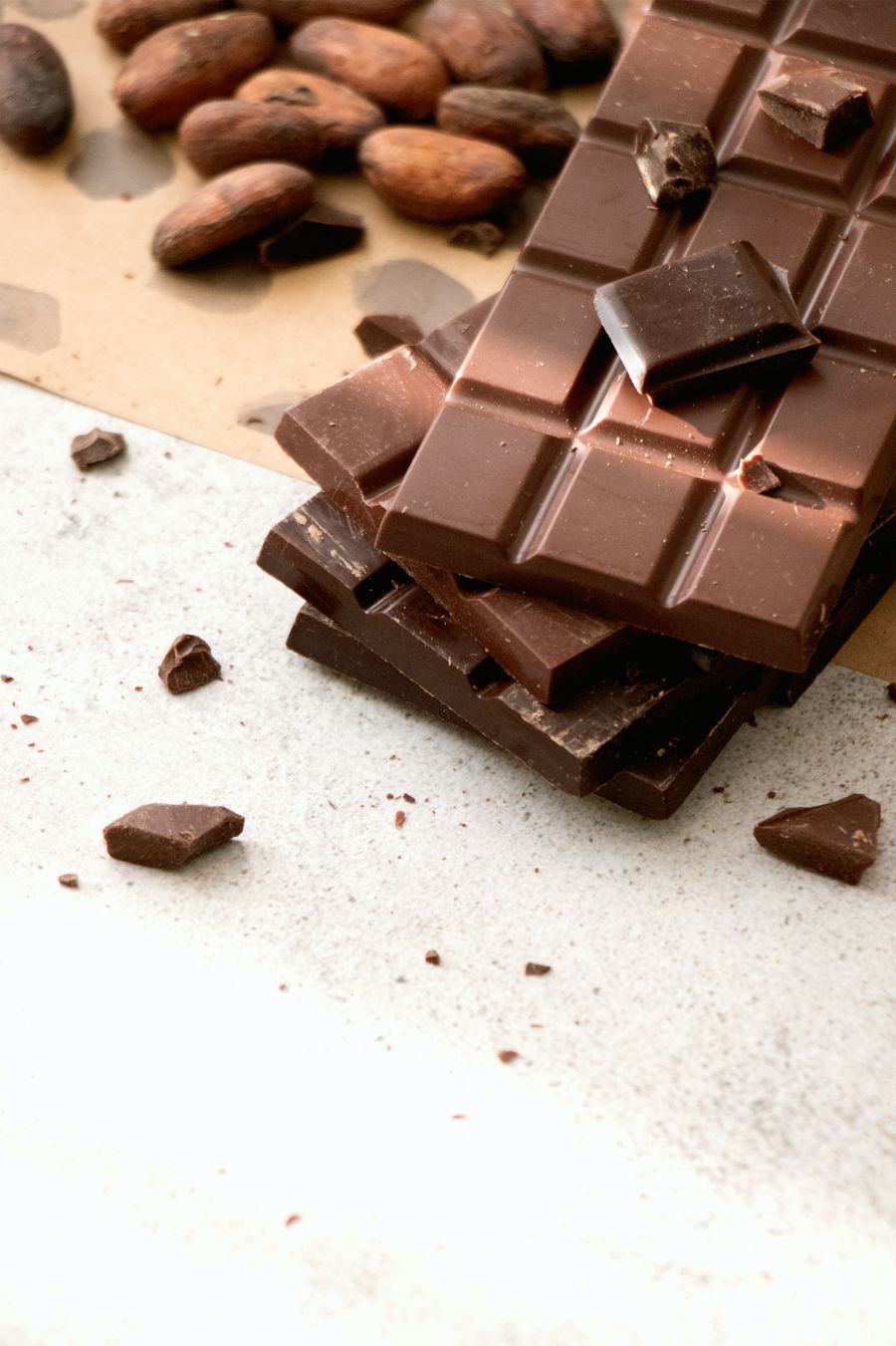 Broken chocolate bars with cocoa beans on a light surface