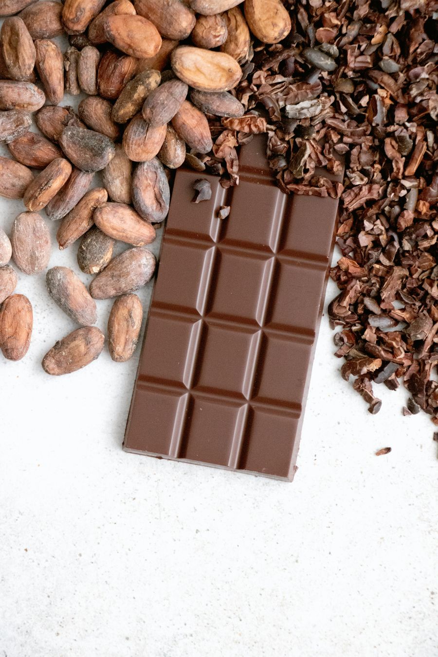 A chocolate bar alongside whole cocoa beans and broken cocoa pieces